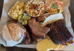 Tray of food at Dayne’s Craft Barbecue in Aledo Texas with brisket ribs sausage OG burger Frito pie beans mac and cheese and street corn