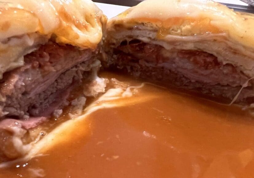 Francesinha sandwich cut open showing layers of meat, sausage and melted cheese with gravy at O Afonso restaurant in Porto Portugal