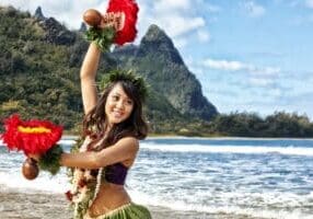 Hula dancer with uli'uli performing at a Kauai luau, with Mount Makana rising behind her on the North Shore